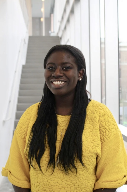 Woman in yellow shirt smiling and standing at bottom of staircase