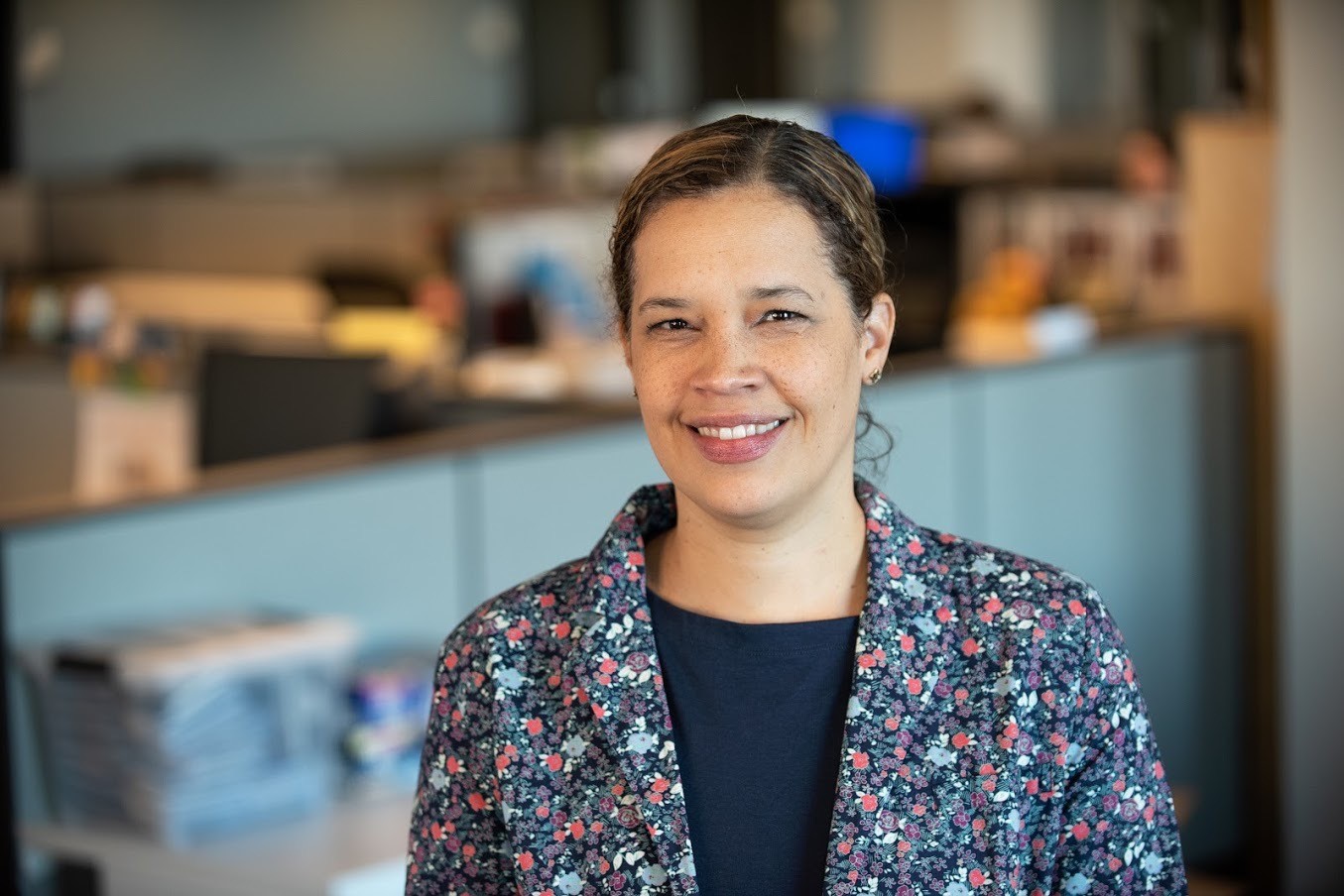 Smiling woman wearing a floral jacket and navy shirt standing in an office.