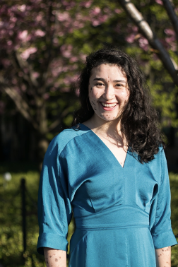 Smiling woman wearing a blue dress with trees in the background.